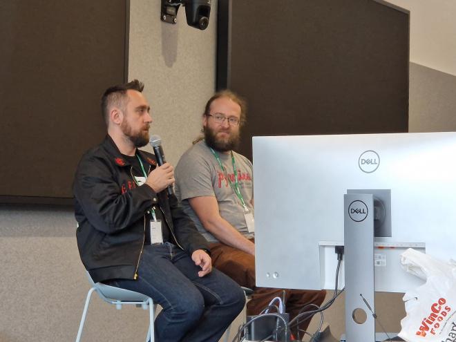 Łukasz (with a microphone) and Petr sitting on high stools.