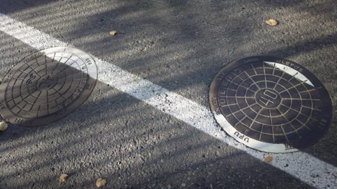 A circular manhole cover that has had a white line painted over one edge, but then lifted up, and rotated 180 degrees before being replaced, so the line is discontinuous.