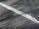 A circular manhole cover that has had a white line painted over one edge, but then lifted up, and rotated 180 degrees before being replaced, so the line is discontinuous.