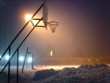 An atmospheric photo of a backlit basketball basket above heaps of snow.