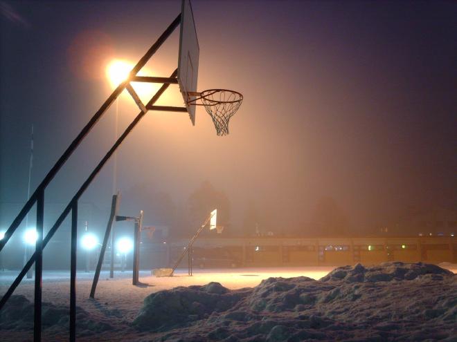 An atmospheric photo of a backlit basketball basket above heaps of snow.